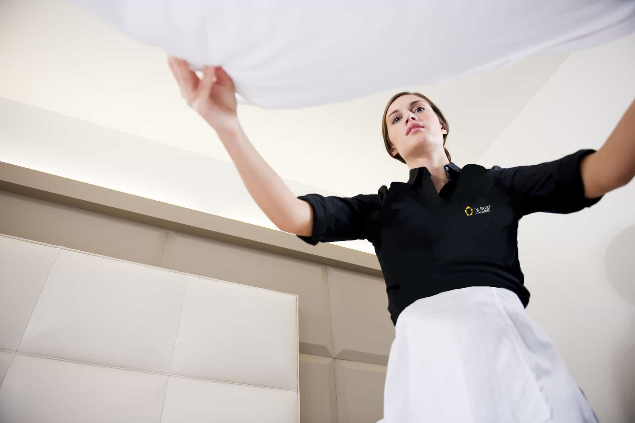 Maid making bed in hotel room