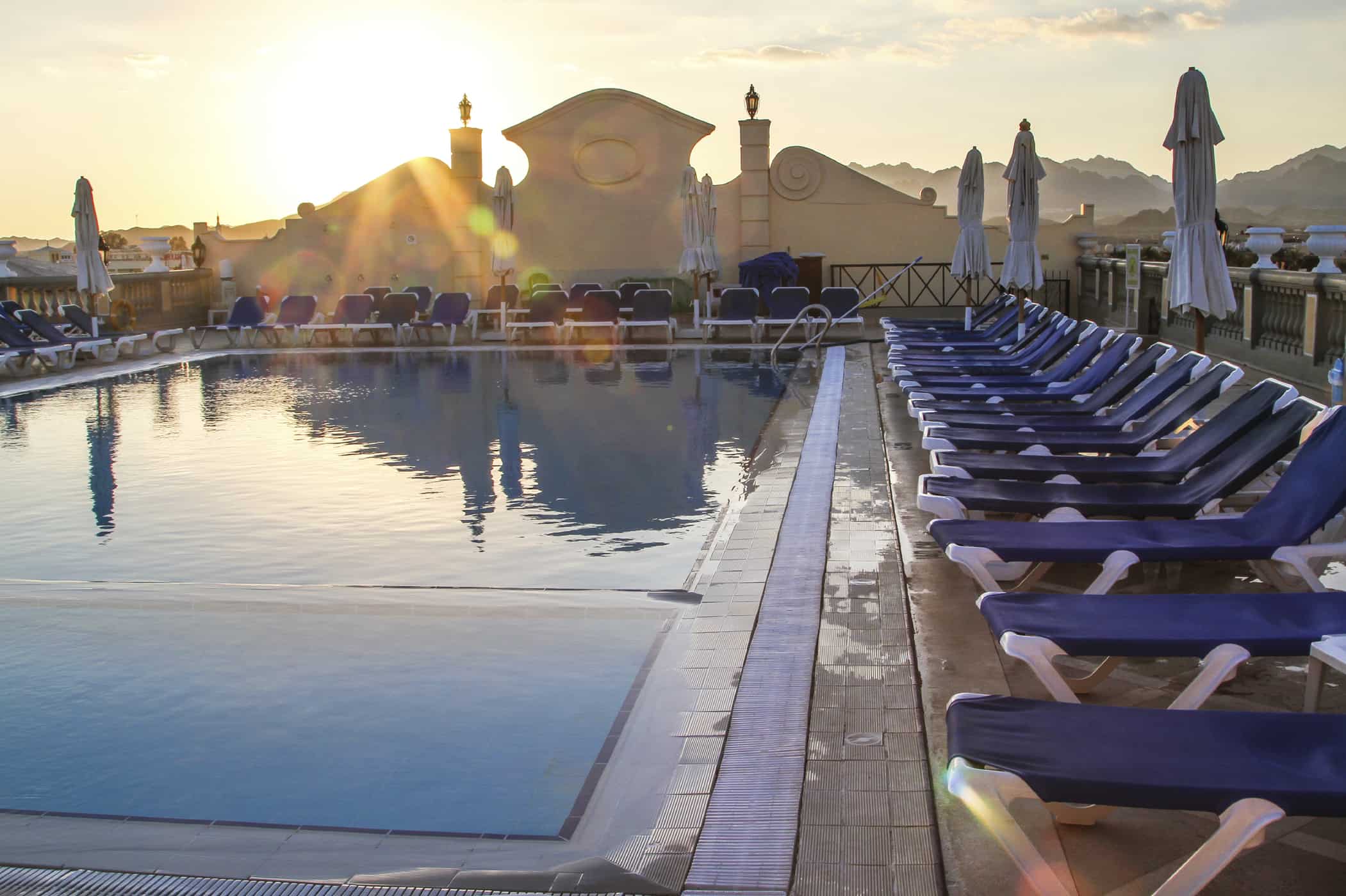 Rectangular pool surrounded by pool chairs at sunset