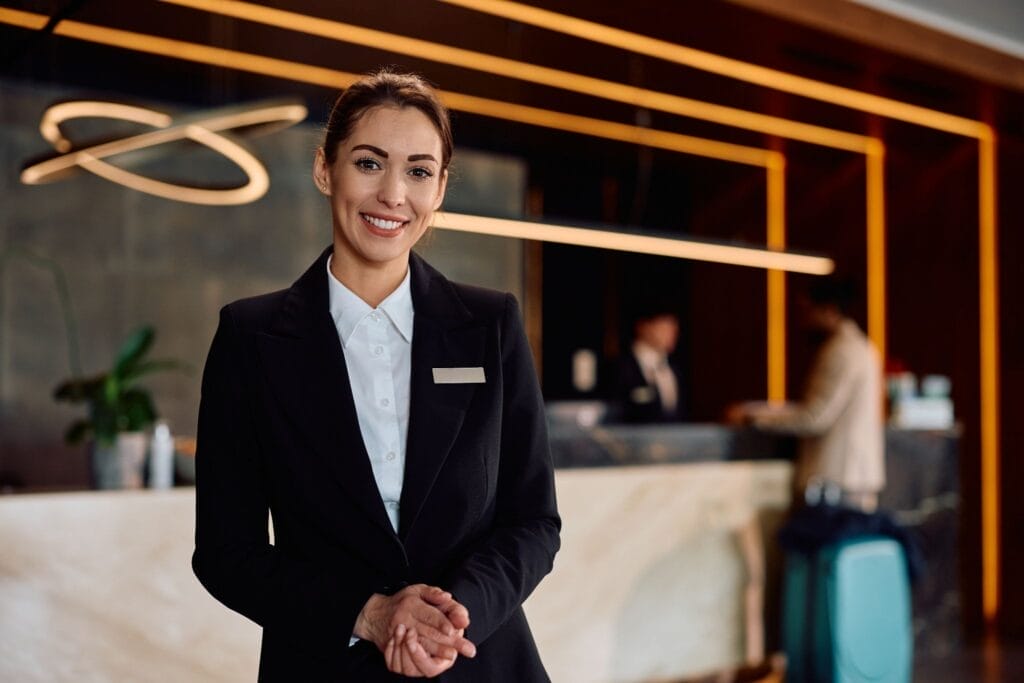 Hotel employee smiling in front of the hotel lobby front desk.
